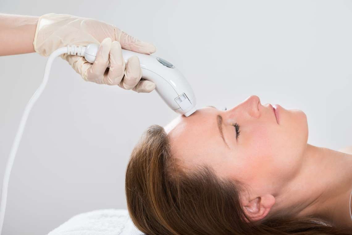 Woman receiving professional Laser Hair Removal Treatment Toronto on her forehead with a handheld device