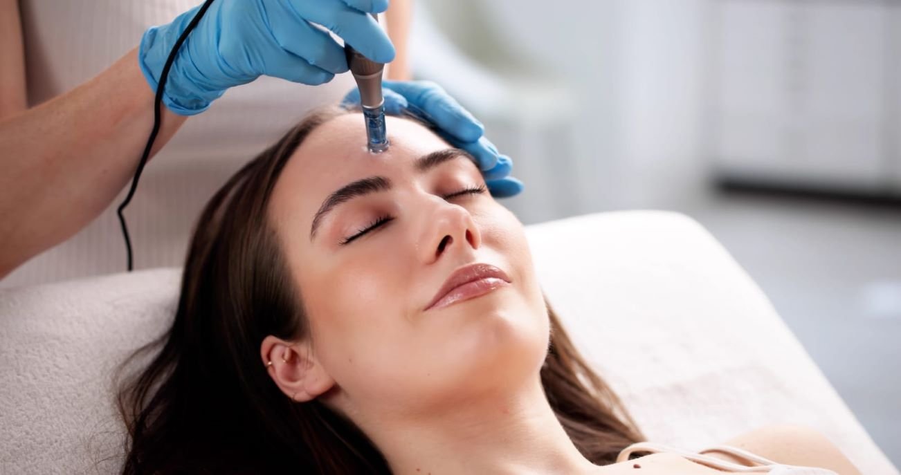 Woman receiving a professional microneedling treatment on her forehead at a skincare clinic.
