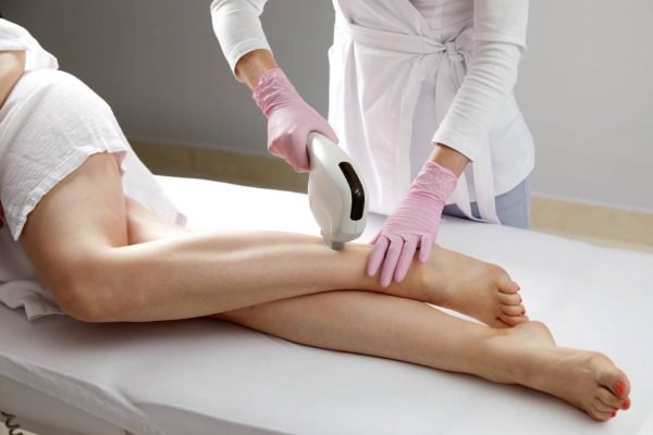 Aesthetician performing laser hair removal on a woman's legs for smooth skin.