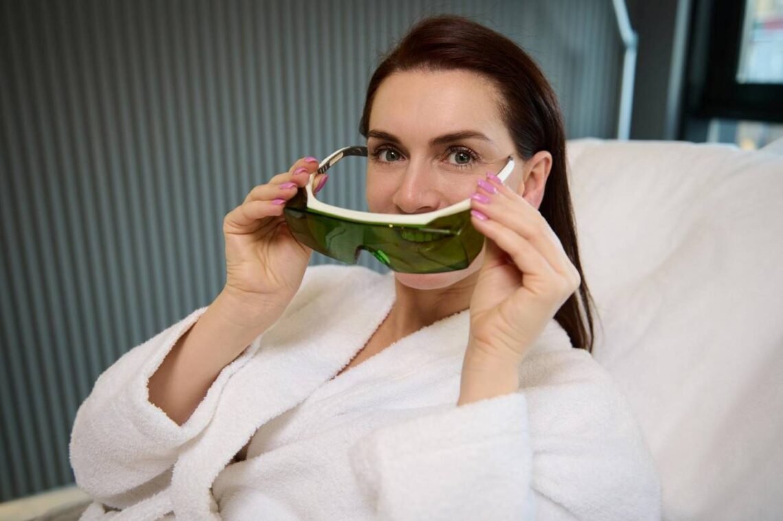 Woman in a white robe holding protective green goggles before a Laser Skin Treatments.